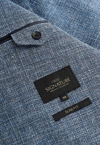 Tissu texturé bleu, coupe ajustée, doté d'un bouton noir, d'un bord foncé contrastant et d'étiquettes "next SIGNATURE" et "SLIM FIT".