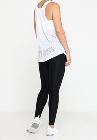 Witte mouwloze tanktop met de tekst "Just Do It" op de rug, gecombineerd met zwarte leggings en witte sportschoenen. Soepele stof, comfortabele pasvorm.
