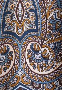 Motif de tissu complexe avec des formes florales et géométriques en bleu, marron, blanc et jaune moutarde.