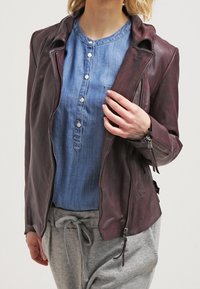 Bordeaux läderjacka med en figurnära design, dragkedjeslutning och accentstygn. Bärs över en blå chambrayskjorta och grå sweatpants.