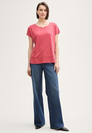 Rosa kortermet topp med en lett scoop-hals, kombinert med vide dongeribukser i mørk denim og spisse svarte sko. Glatt stofftekstur.