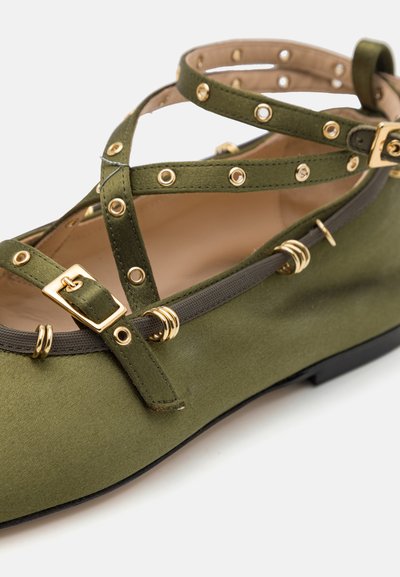 Green satin flats with crisscross straps, gold hardware accents, and stud detailing. Flat, rounded toe with a textured surface.