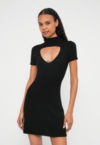 Rochie neagră cu dungi, cu guler înalt și o decupare masivă în formă de V la piept. Mâneci scurte, siluetă ajustată și țesătură texturată.