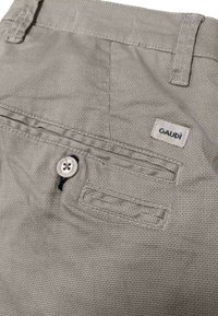 Pantaloni corti di tessuto beige con una trama testurizzata, dotati di una tasca posteriore con bottone e di un'etichetta tessuta con la scritta "GAUDI."