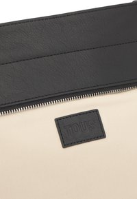 Czarna skórzana kopertówka o fakturowanym wykończeniu, z kontrastującym beżowym korpusem, srebrnym zamkiem błyskawicznym i czarną naszywką z wytłoczonym logo.