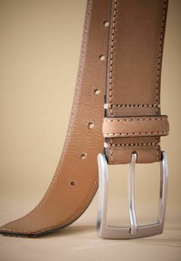 Ceinture en cuir couleur tan avec une texture lisse, boucle rectangulaire argentée et coutures visibles. Possède des trous pour les ajustements sur toute sa longueur.