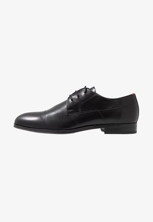 Chaussure habillée pour homme en cuir noir avec bout rapporté, trois œillets pour lacets et talon bas empilé, vue de profil droit sur fond blanc.