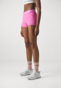 Lyserøde Nike Pro shorts med en bred talje, parret med hvide sneakers og lyserøde sokker med 'Nike' tekst. Glat, strækbart materiale.