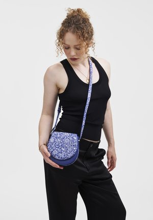 Blue floral pattern crossbody bag with a semi-circular shape, accented by a solid blue bottom and a decorative strap.