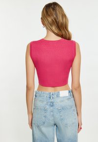 Feszes, ujj nélküli, bordás cropped top élénk rózsaszínben, világoskék, magas derekú farmernadrággal párosítva, hátsó zsebekkel és enyhe fakulással.