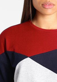 Jersey color bloqueado en rojo, azul marino y gris con cuello redondo; fabricado en una tela suave y con patrones geométricos distintivos.