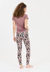 Top mauve à manches courtes avec un design fluide, associé à un legging noir avec un motif floral dans des tons rose et crème.