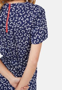 Robe bleu marine avec motif floral blanc, taille élastique et manches courtes. Fermeture zip au dos avec détail en rouge. Tissu doux, coupe décontractée.