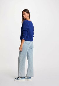 Maglione blu lavorato a maglia con dettagli nei polsini e vestibilità morbida. Abbinato a jeans a gamba larga blu chiaro e sneakers blu con dettagli bianchi.