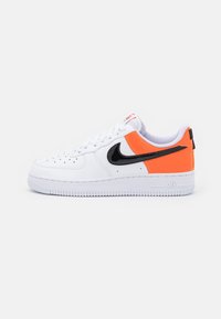 Vita lädersneaker med orange och svart accent, perforeringar på tån och en texturerad gummisula med "AIR"-logotyp.