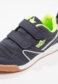 Marineblaue Sportschuhe aus strukturiertem Stoff, mit weißen Akzenten und neongrüner Innenausstattung. Verfügt über zwei Klettverschlüsse und eine Gummisohle.