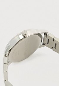Montre-bracelet Calvin Klein en métal argenté, montrant le boîtier arrière lisse et le bracelet à maillons ajustable sur un fond clair.