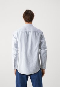 Camisa blanca de manga larga con dobladillo curvado y puños de un solo botón, con una pequeña etiqueta de logo en la parte trasera del cuello, hecha de una tela texturizada.