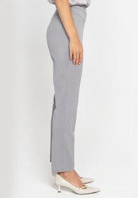 Szare, dopasowane spodnie o prostym kroju, z gładką teksturą materiału i bocznymi rozcięciami. Zestawione z białymi szpilkami z wydłużonym noskiem.