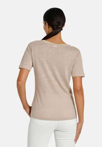 Beige T-Shirt mit kurzen Ärmeln, aus einem weichen, leichten Material gefertigt. Es hat einen lockeren Schnitt und einen runden Halsausschnitt mit einer dezenten Textur.