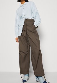 Jasnoniebieska koszula z kołnierzykiem, zestawiona z brązowymi, luźnymi spodniami z boczną kieszenią na zamek i detalami ze sznurkiem.