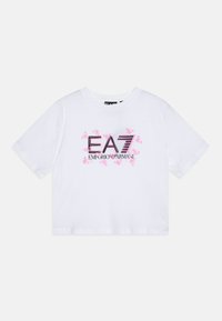 Fehér, pamutból készült cropped t-shirt, amelyen a "EA7 EMPORIO ARMANI" logó rózsaszín és fekete színben látható, rövid ujjaival és kerek nyakkivágásával.