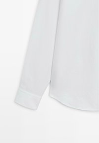 Weißes Langarmhemd mit abgerundetem Saum, ausgestattet mit einem knöpfbaren Manschette und glatter Stoffstruktur. Einfaches Design, ohne Muster oder Verzierungen.