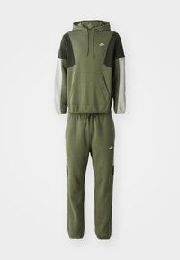 Olíva zöld Nike kapucnis pulóver szürke és zöld részletekkel, hozzá illő melegítőnadrággal, elöl zsebbel és rugalmas derékkal.