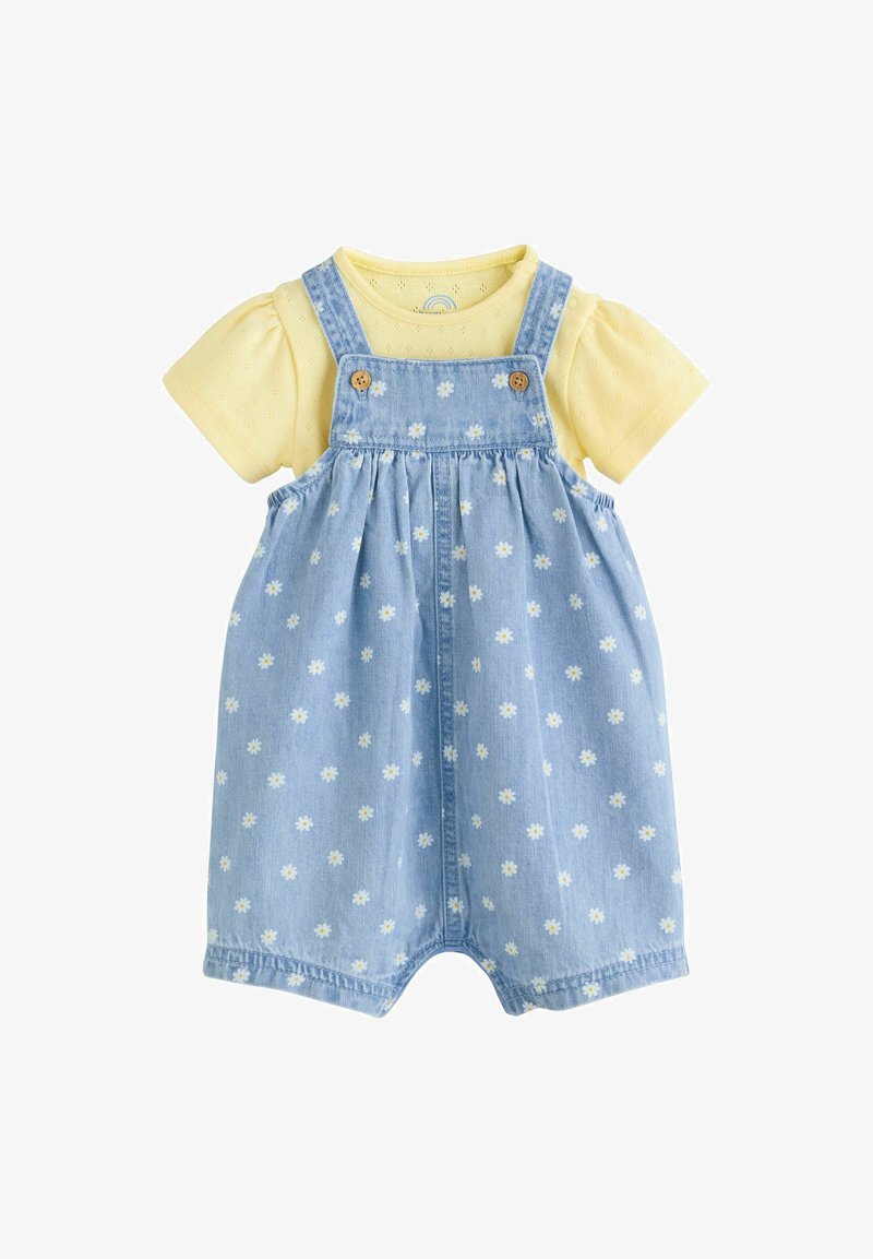 Jasnoniebieska sukienka ogrodniczka z dżinsu z żółtą koszulą z krótkim rękawem. Ogrodniczka zdobiona jest białym nadrukiem stokrotek i drewnianymi guzikami; wykonana z miękkiej bawełny.