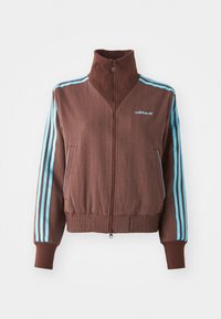 Ruda zip-up striukė su gumine tekstūra, turinti turkio spalvos tris juosteles ant pečių ir rankovių bei siuvinėtą logotipą.