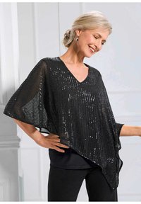 Schwarzer Pailletten-Poncho mit V-Ausschnitt, fließenden Ärmeln und lockerer Passform, über einem schwarzen Oberteil getragen und mit schwarzen Hosen kombiniert.