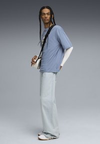Blå bomulds t-shirt lagd over en hvid langærmet skjorte, parret med lyse denim jeans og hvide sneakers. Sort crossbody taske i hånden.