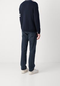 Mörkblå stickad tröja med vita ränder på ärmarna, tillsammans med mörkblå jeans och off-white sneakers, sedd bakifrån.