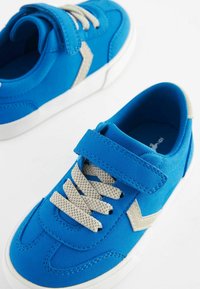 Niebieskie sneakersy z teksturowaną cholewką, z rzepem, jasnoszarymi sznurówkami i białymi gumowymi podeszwami o prostym wzorze.