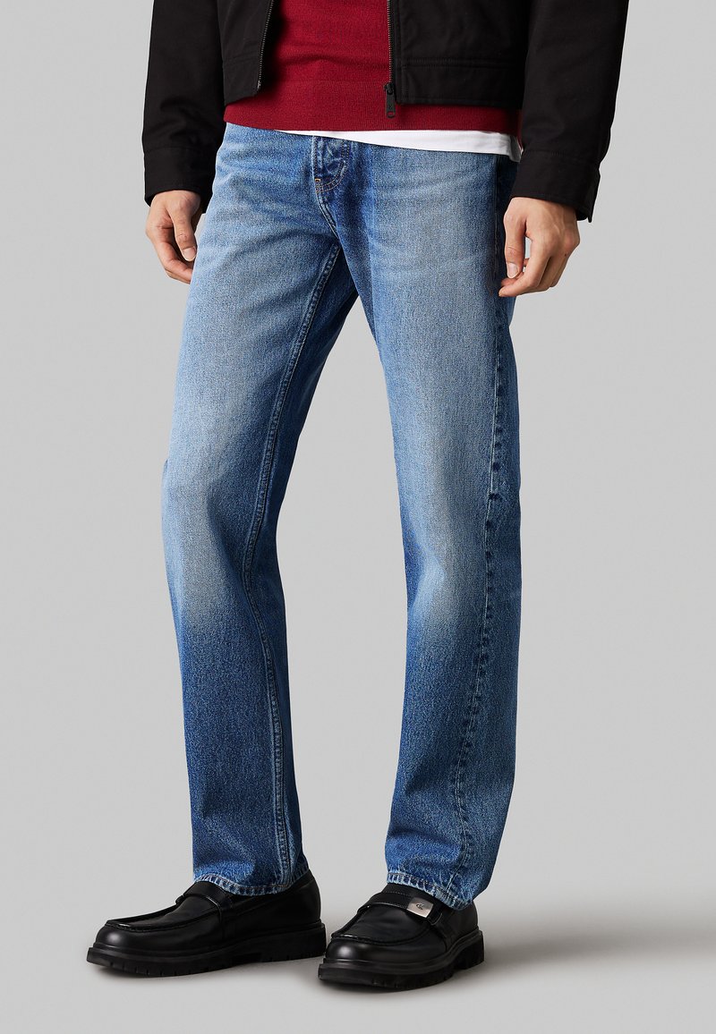 Jeans in denim blu chiaro con design a gamba dritta, texture sbiadita e stile tradizionale a cinque tasche. Indossati con mocassini neri.