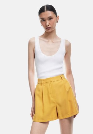 Un débardeur blanc côtelé associé à un short plissé jaune vif taille haute. Textures de tissu lisses, design simple sans motifs.