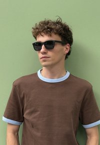Hnědý tričko s krátkým rukávem a světle modrými manžetami a límcem. Černé sluneční brýle. Kadeřavé vlasy. Jednoduchý design s uvolněným střihem.
