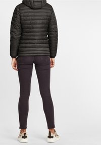 Czarna kurtka puchowa z kapturem, zestawiona z ciemnofioletowymi dżinsami typu skinny. Obuwie ma jasną podeszwę z dodatkami w odcieniach brązu i beżu.