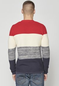 Maglione a righe rosse, crema, grigie e blu navy in un tessuto a coste, con maniche lunghe, collo rotondo e un design aderente.