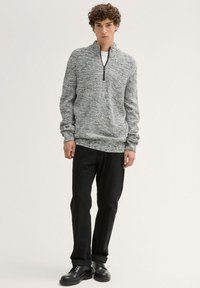 Gilet zippé en tricot gris et noir avec un motif texturé ; associé à un jean noir et des bottes à lacets noires.