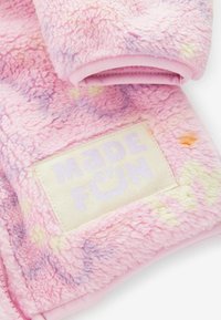 Różowy, miękki materiał z pastelowymi wzorami tie-dye i naszytą prostokątną metką z napisem „Made of Fun” w jasnofioletowym kolorze.