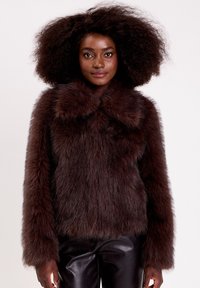 Veste en fausse fourrure marron avec un large col, surface texturée, manches longues et coupe droite, accompagnée de pantalons en cuir noirs.