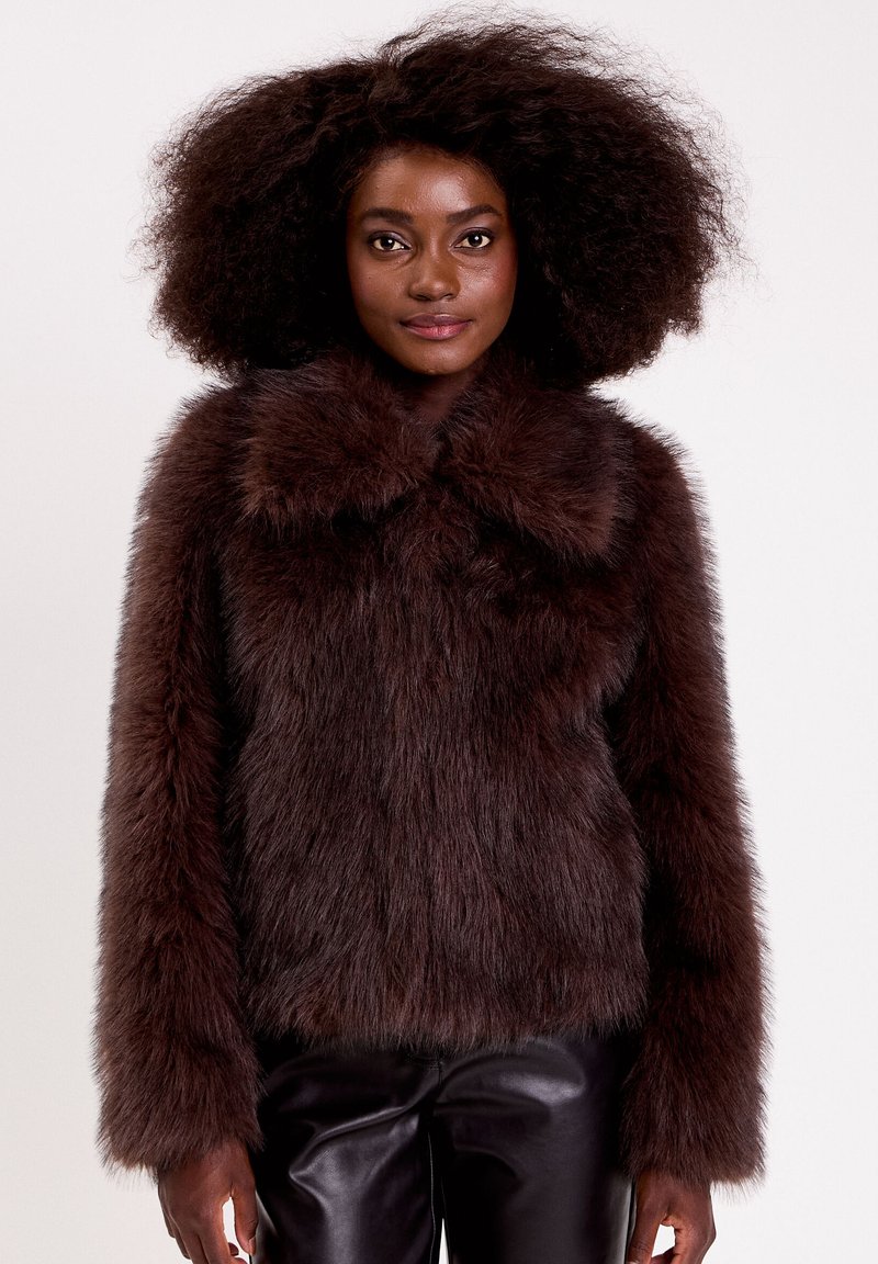 Veste en fausse fourrure marron avec un large col, surface texturée, manches longues et coupe droite, accompagnée de pantalons en cuir noirs.