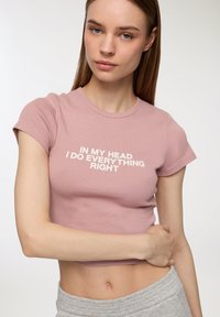 T-shirt cropped rosa con maniche corte e testo bianco che recita "Nella mia testa faccio tutto giusto". Materiale in cotone morbido, design slim.