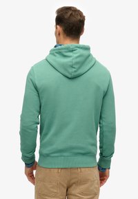 Sudadera de algodón verde con capucha ajustable, puños acanalados y dobladillo. Textura suave con un corte ajustado.