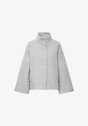 Hallikas villasegu jakk kõrge kraega, lõdva istuvuse, kahe esise tasku ja nähtavate sulgude või kaunistusteta.