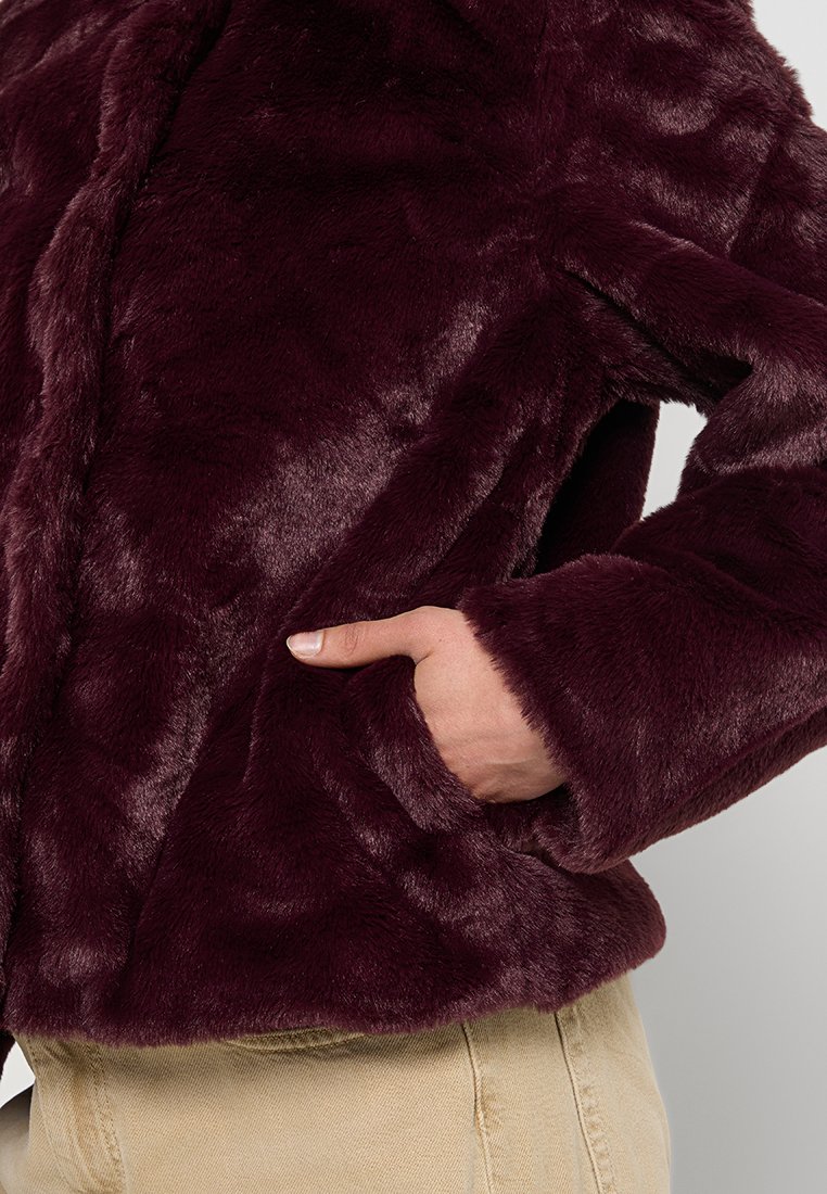 Giacca in pelliccia sintetica bordeaux con finitura testurizzata, dotata di tasche laterali e un taglio rilassato. Il materiale morbido e la lucentezza delicata esaltano il design.