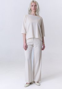 Beige lockere Oberteil mit kurzen Ärmeln, kombiniert mit hochtaillierten, weiten Hosen und strukturierten hellen Schuhen. Einfaches, minimalistisches Design.