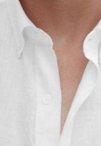 Vit linneskjorta med knappkrage och knappslå. Närbild som visar mjuk struktur och detaljer i kragen.
