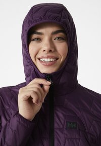 Fialová nadýchaná bunda s kapucí, s geometrickým prošívaným vzorem a zipovým zapínáním. Nášivka loga na levé straně. Hladká, lesklá textura.